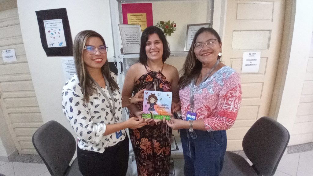 Assistentes sociais do IPMB, Gisele Batalha e Heloisa Pinto recebem livro doado por Uendy Feitosa (centro)